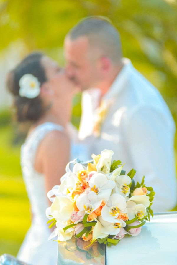 groom and bride kissing at the back of floral bouquet