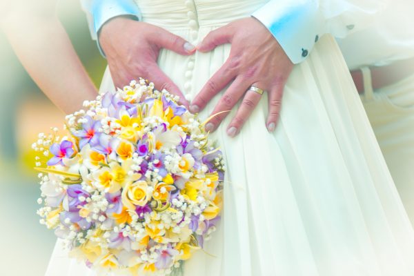 creative shot of groom forming a heart with hands with floral bouquet