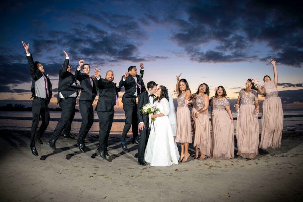Group photo of the bride, her bridesmaids, the groom, and his groomsmen jumping at the beach in Mauritius at sunset, beautiful sky 
