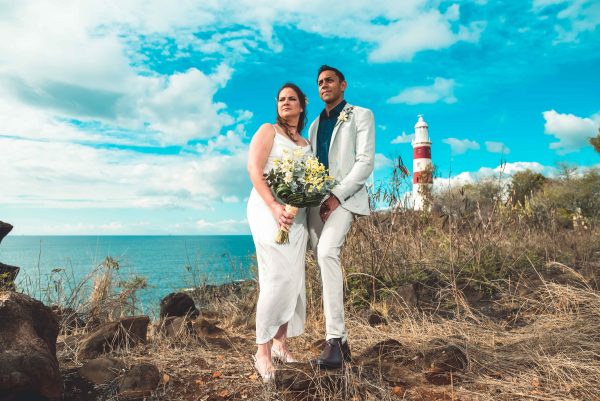 A couple is posing near a cliff with the lighthouse in a distance 